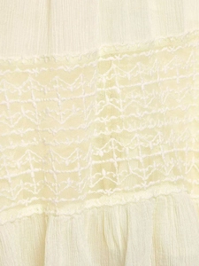 Detail of pleated beige chiffon fabric featuring intricate lace embroidery and ruffled edges