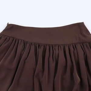 Detail shot of a dark brown pleated skirt showing high waist design and hidden zipper
