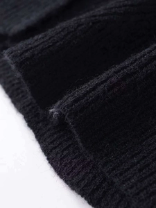 Close-up detail of the black knitted cardigan featuring a ribbed hem and soft wool texture