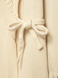 Detail of a cream knit cardigan featuring a soft ribbon tie bow and textured fabric