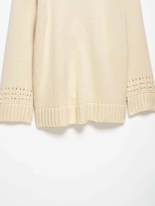 Detail of cream knit cardigan featuring scalloped lace cuffs and ribbed hemline texture