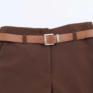 Dettaglio dei pantaloni marrone scuro con cintura in pelle marrone e fibbia dorata