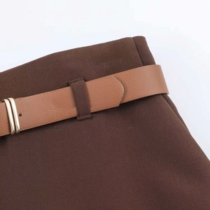 Dettaglio dei pantaloni marroni a gamba larga con cintura in pelle e fibbia dorata a doppio anello