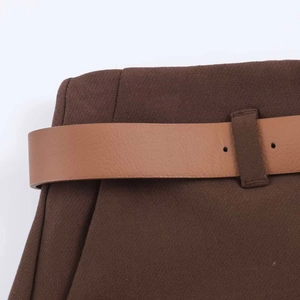 Dettaglio dei pantaloni a gamba larga a vita alta con una sottile cintura in pelle marrone chic