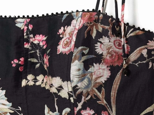 Detailed view of floral print dress with thin straps, bead charms and ruffled trim edge