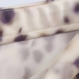 Detailed close-up of smooth satin fabric with purple tie-dye patterns and fine stitching