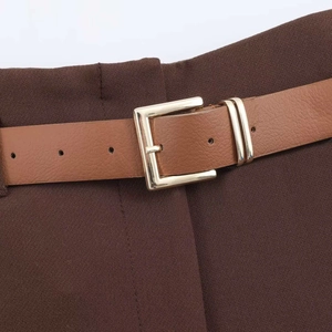 Dettaglio di pantaloni larghi marrone scuro con cintura in pelle e fibbia dorata