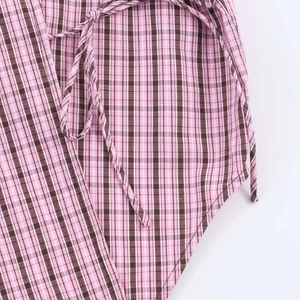 Detail of pink and brown gingham top featuring a waist tie and curved hem split