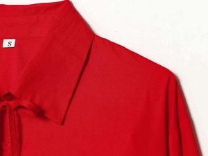 Detail of red bow-tie blouse showing twill fabric texture and white size S neck label