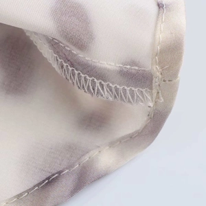 Macro shot of fine overlock stitching and grey-white tie-dye satin fabric texture