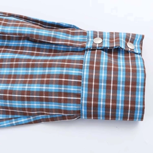 Close-up of blue and brown plaid shirt cuff featuring dual round silver metal buttons