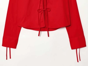 Detailed view of red long-sleeve shirt featuring decorative bow ties and cuff ribbons