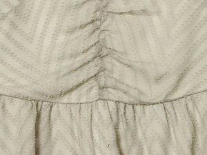 Detailed close-up of light apricot pleated fabric with Swiss dots and ruched stitching detail