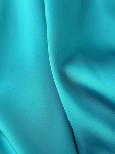Detail of teal satin fabric with twill texture and elegant draping on asymmetric dress