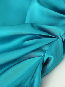 Close-up of peacock blue satin fabric featuring elegant ruffled pleats and silky texture
