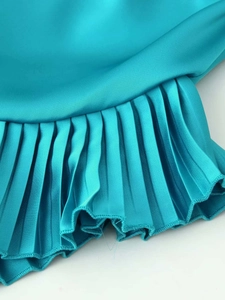 Detailed macro view of pleated satin hem on this elegant green one-shoulder dress
