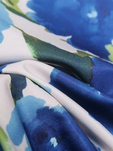 Detailed close-up of white satin fabric with large blue floral prints and green leaves