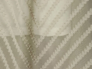 Close-up of beige pleated fabric featuring V-shaped texture and decorative 3D dots