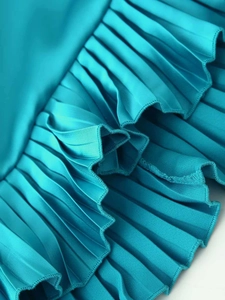 Detailed macro view of pleated fabric and ruffled hem on a teal asymmetrical dress