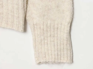 Detailed close-up of cream knit sweater with soft wool texture and ribbed cuffs