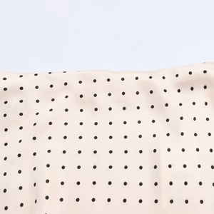 Detailed view of polka dot pattern on soft apricot satin fabric for asymmetric midi skirt