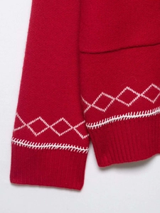 Close-up of red knit cardigan featuring white geometric diamond patterns and ribbed cuffs