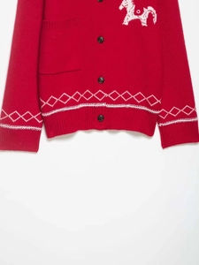 Detail view of red knit cardigan featuring white horse pattern and diamond pattern cuffs