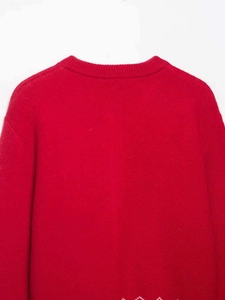 Détail d'un pull en maille rouge avec col rond et motif de flocons de neige blancs