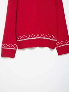 Détail d'un pull en maille rouge avec broderie losange blanche et bordure côtelée