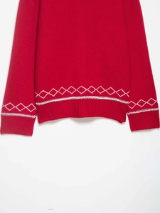 Detail view of red knit cardigan featuring white geometric jacquard on ribbed hem and cuffs