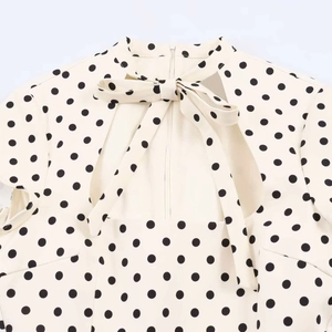 Detail of white polka dot dress featuring high neck bow tie and chest cutout design
