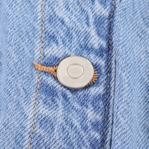 Macro view of light blue denim fabric with orange double stitching and silver metal button