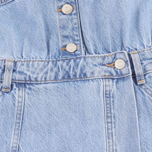 Detail of waist stitching, metal buttons, and denim texture on light blue mini dress