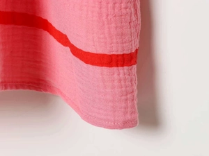 Dettaglio di un abito estivo a righe rosa e rosse in tessuto di cotone crepe testurizzato