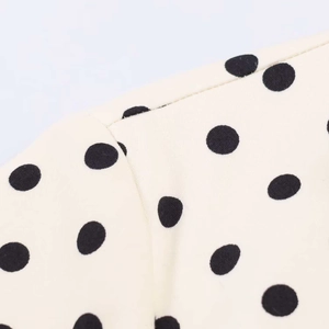 Macro detail of summer dress featuring black polka dots on cream woven fabric