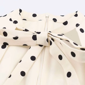 Detail of beige polka dot dress featuring a bow tie and invisible zipper closure