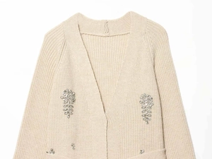 Detailed macro view of beige knit cardigan featuring crystal floral beadwork and soft texture