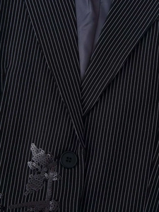 Macro detail of black pinstripe blazer featuring sequin floral embroidery and button closure