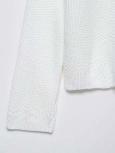 Detail of white high-neck knit sweater featuring chunky knit texture and side split hem