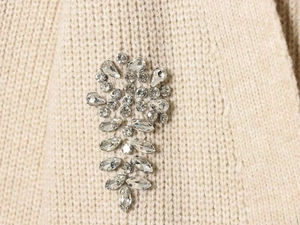 Detailed view of hand-sewn crystal beads and rhinestones on a beige knit cardigan sweater
