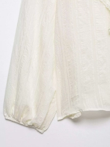 Détail de chemise blanche à manches longues avec texture rayée et bordure en dentelle