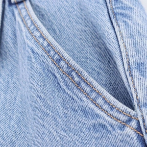 Detailed macro view of light blue denim fabric with reinforced orange double stitching