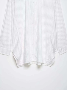 Detail of loose-fit white long-sleeve shirt with fine black vertical stripes and side slits