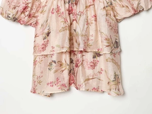Detail of light pink floral summer dress with puff sleeves and ruffled layered hemline
