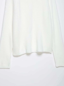 Detail of white chunky knit sweater showing the thick texture and ribbed hem finishing