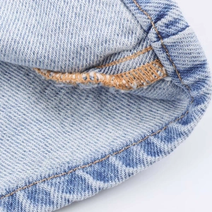 Close-up of light blue denim fabric with high-quality orange double stitching detail
