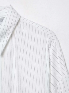 Detailed view of striped cotton fabric texture and neck label on a loose white shirt