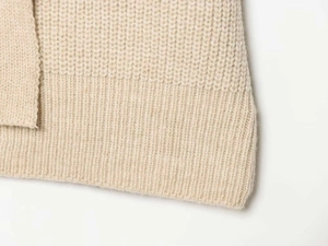 Close-up of beige knit cardigan featuring waffle texture and ribbed hem detailing