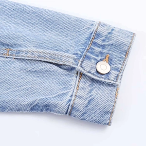Detailed close-up of light blue denim cuff with silver metal button and contrast stitching