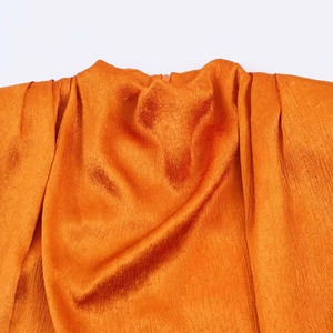 Detail of orange textured pleated fabric featuring a chic stand collar and shoulder folds